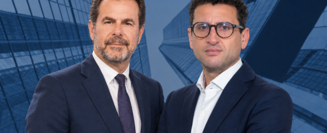 Two businessmen in navy suits pose with arms crossed against a blue glass skyscraper background, looking at the camera in a corporate portrait.